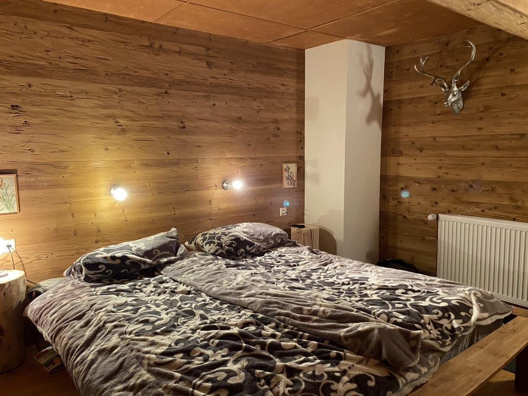 Großes Doppelbett mit grauem Bezug in Schlafzimmer mit Holz