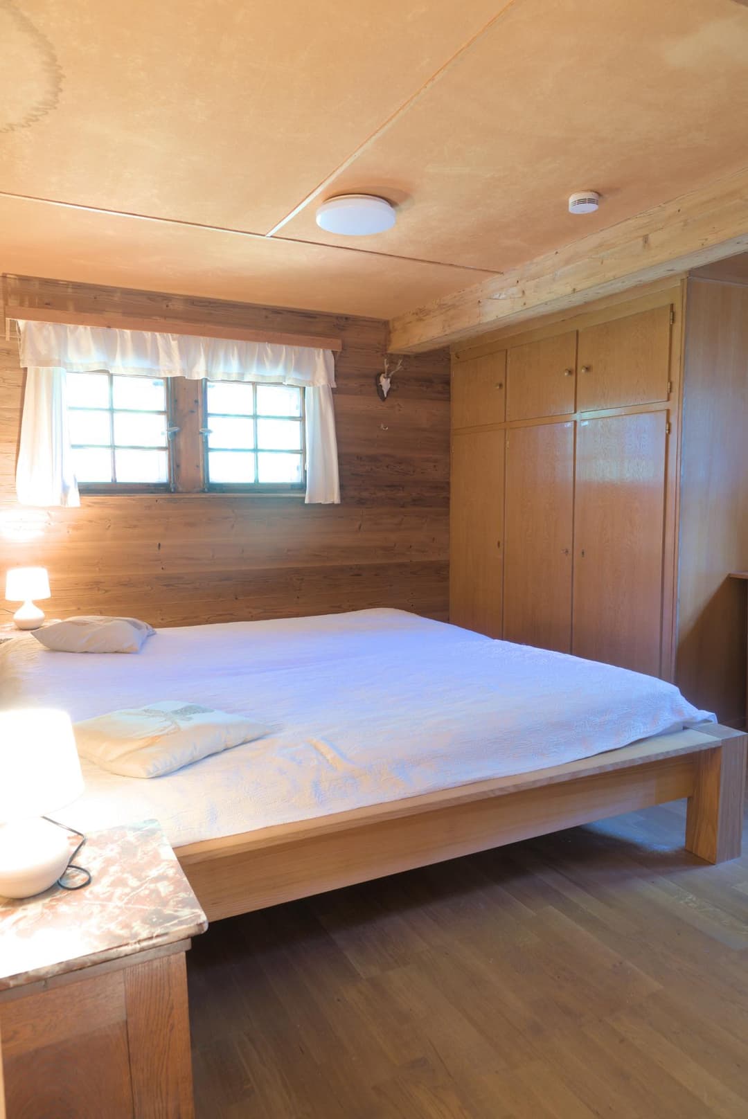 Mittleres Doppelbett mit weißem Bezug vor Holzschrank