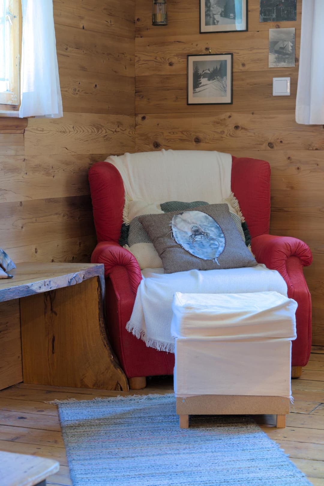 Roter Stoffsessel mit weißen Verzierungen im Wohnzimmer, dazu ein Hocker